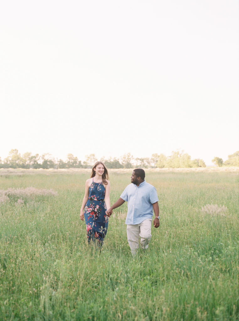 Mixed race couple hold hands while walking in an open field in Princeton