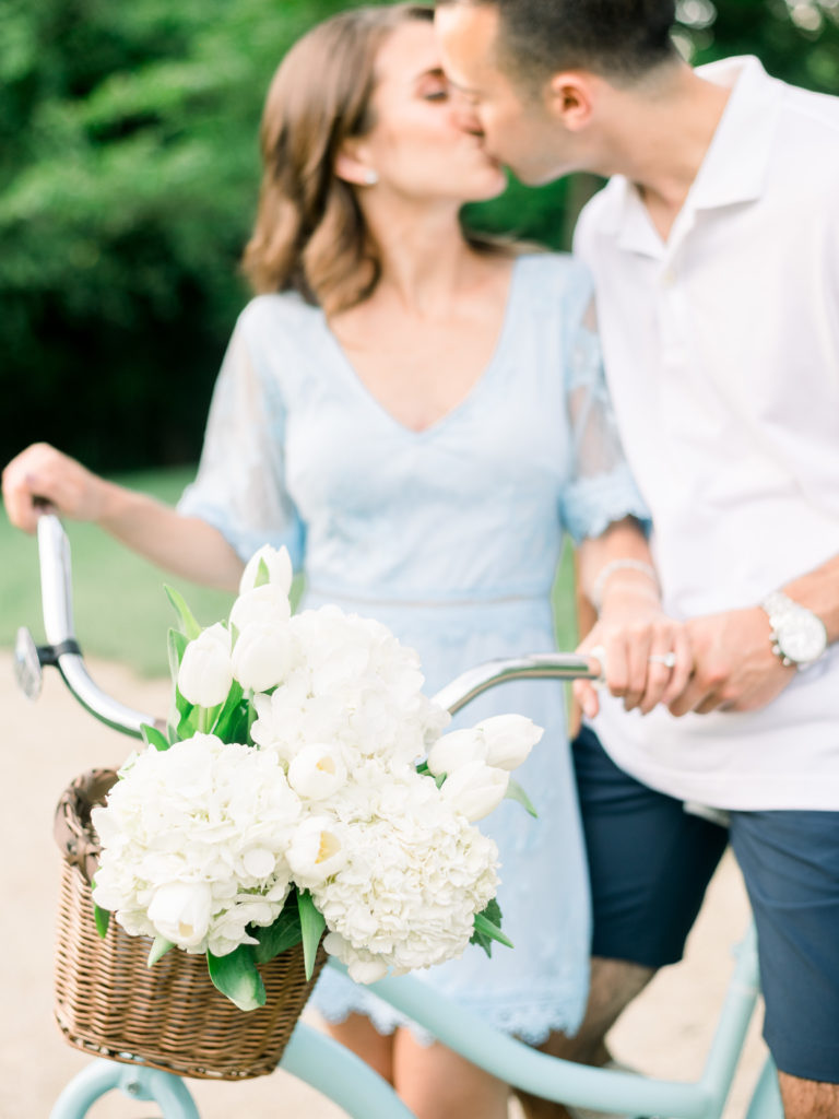 Couple kissing on a vintage bike with flowers at their engagement session at Sayen House and Gardens
