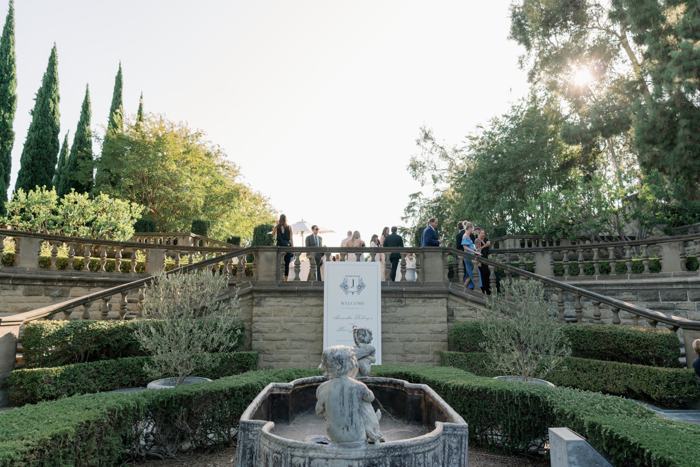 Guests milling atop the stone terrace at Greyview Mansion with an empty fountain in the foreground 