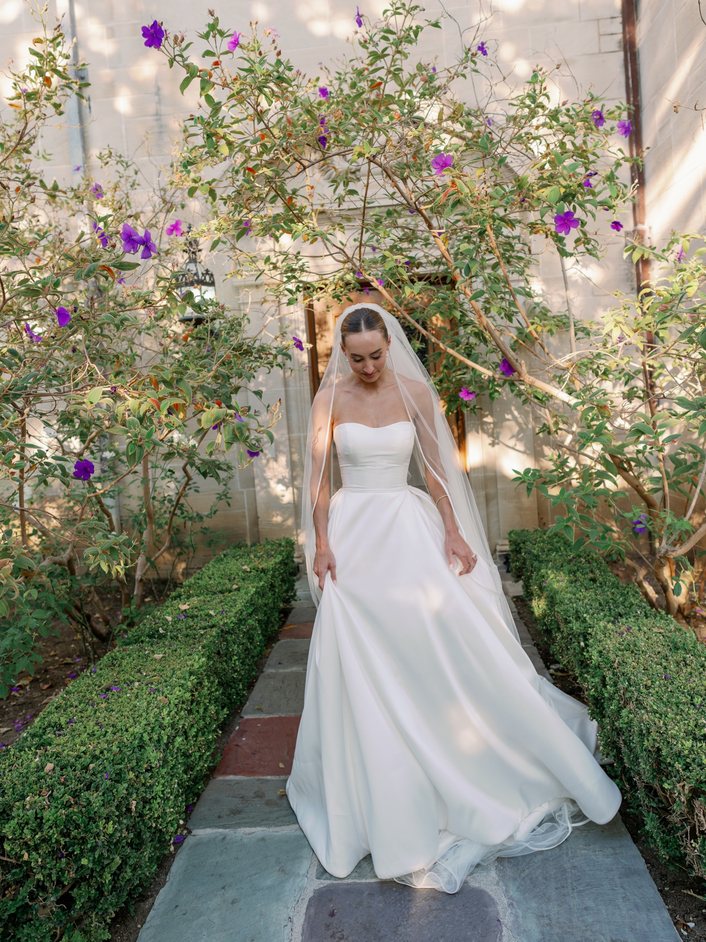 Bride looking down surrounded by trees with sparse purple flowers