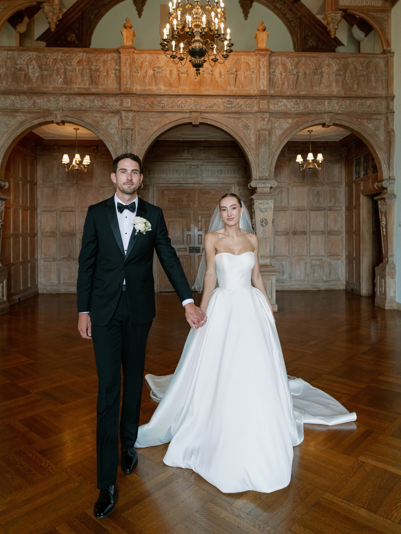 Bride and groom walking in a wood paneled room with arches 