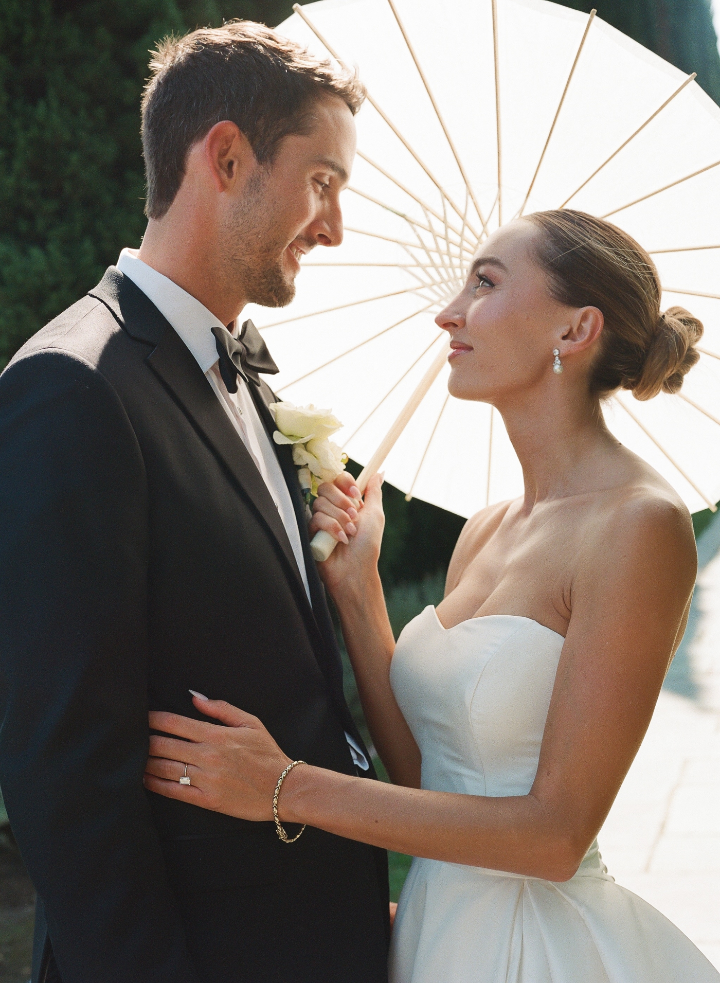 Bride and groom smiling at each other while bride holds a parisol behind them