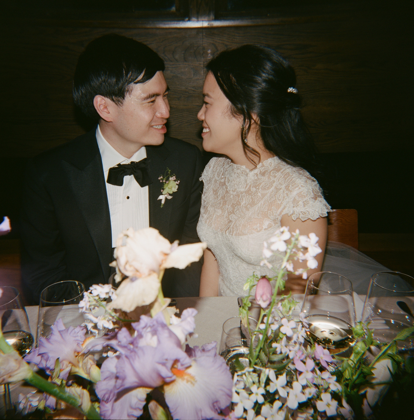 Bride and groom smiling at each other sitting at sweetheart table during wedding reception 