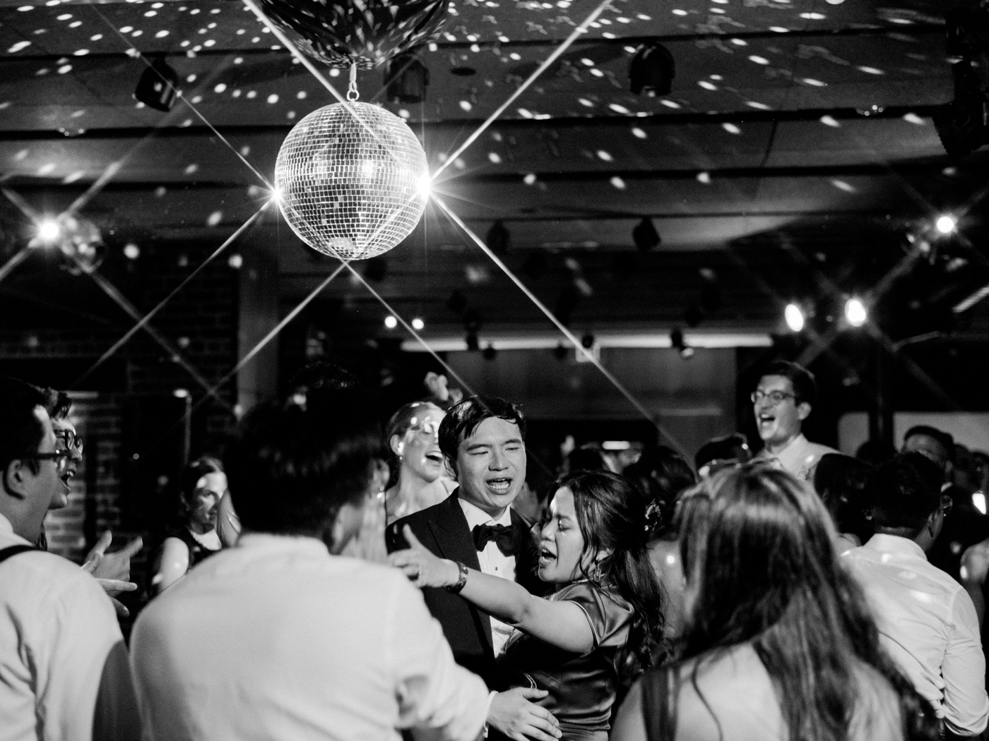 Bride and groom singing surrounded by guests under a disco ball 