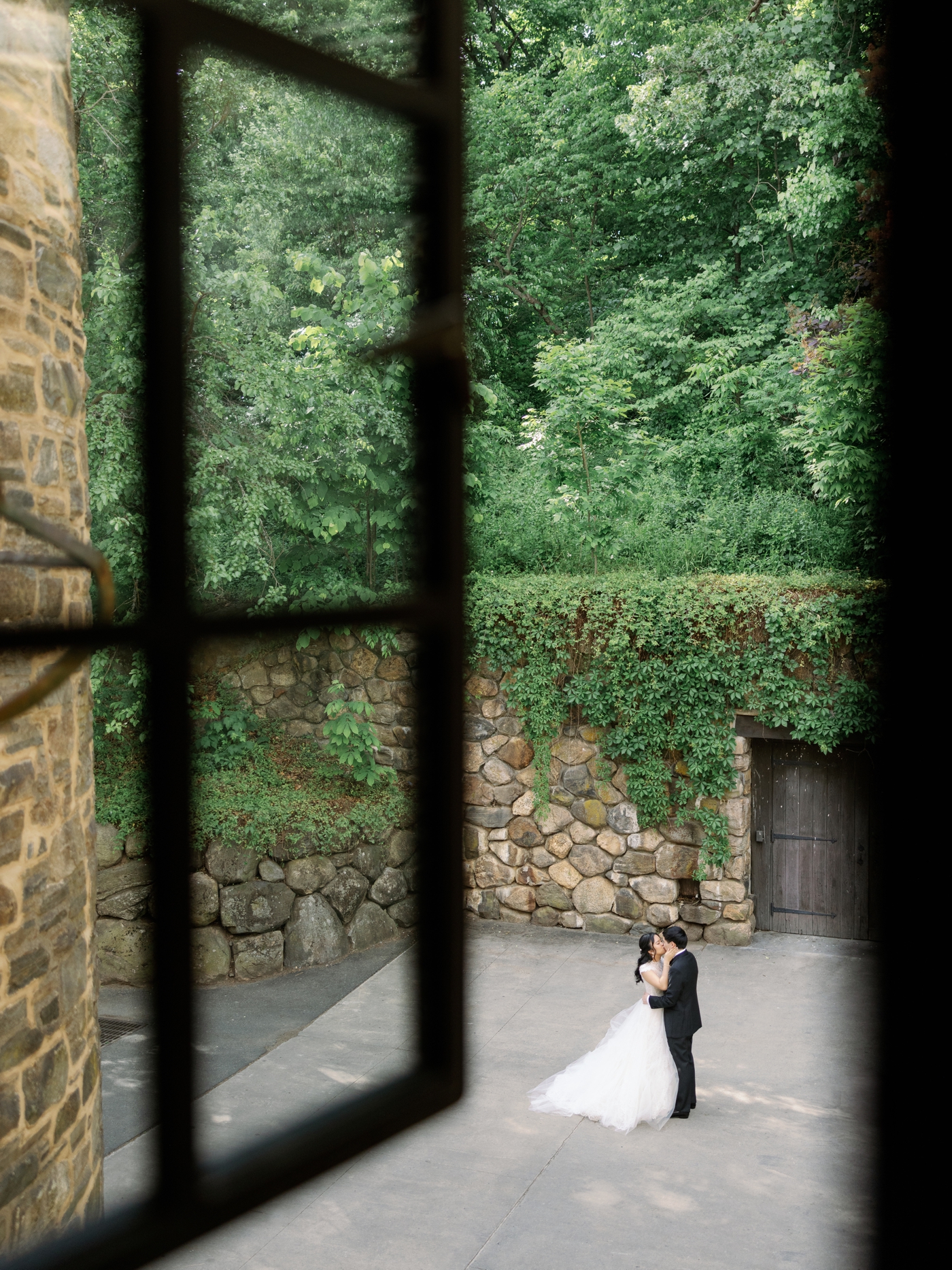 View from a second floor window of bride and groom kissing in a courtyard surrounded by stone walls